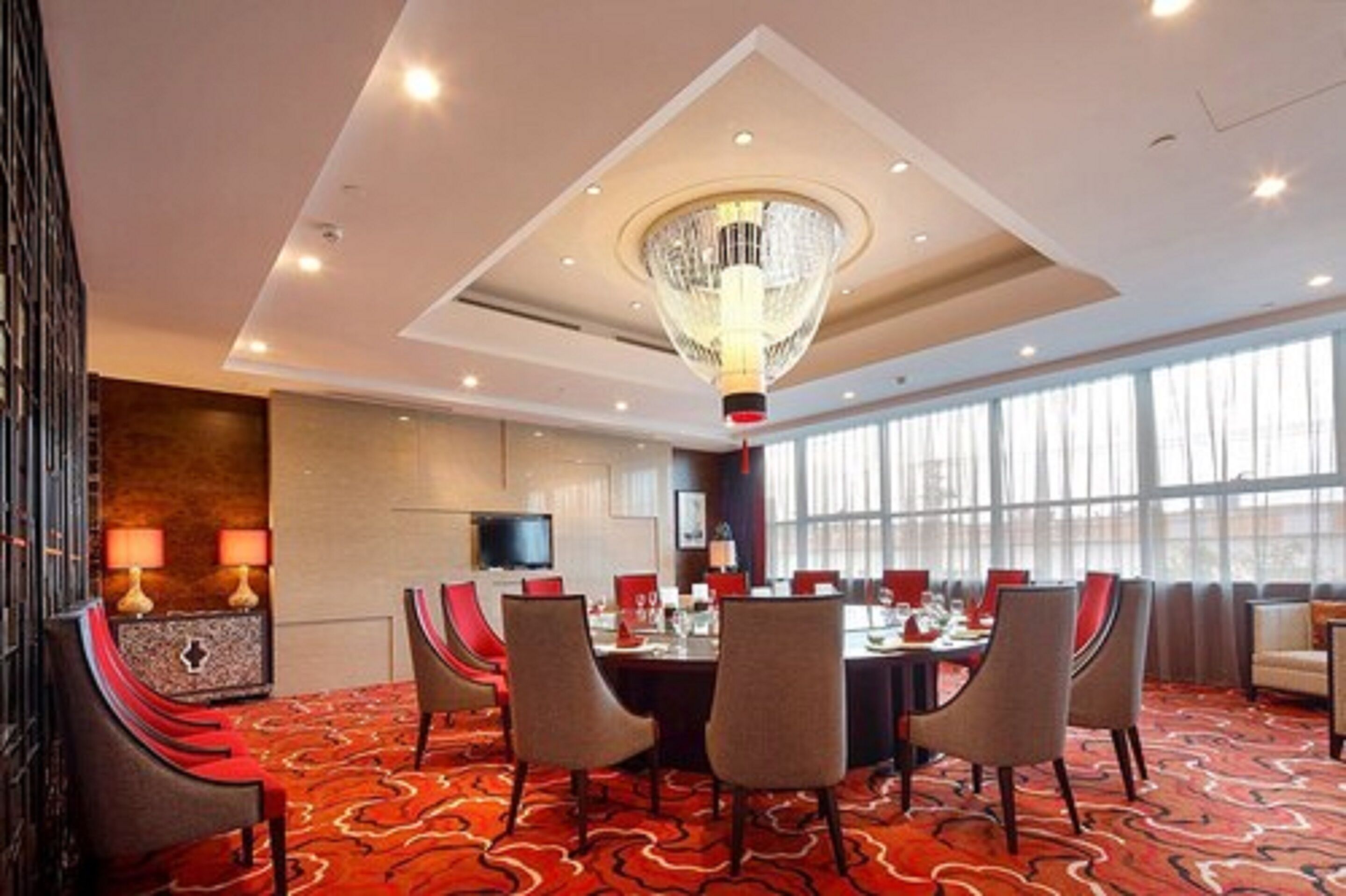 Een hotelconferentiezaal met een lange tafel, meerdere stoelen, een kroonluchter en grote ramen.