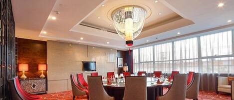 Een hotelconferentiezaal met een lange tafel, meerdere stoelen, een kroonluchter en grote ramen.