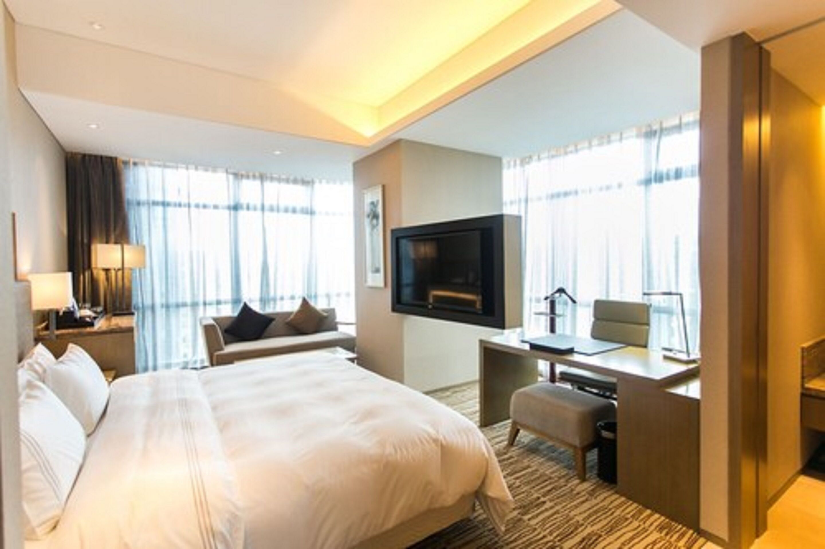 Quarto de hotel com uma cama grande, uma escrivaninha com cadeira, televisão e janela com cortinas.