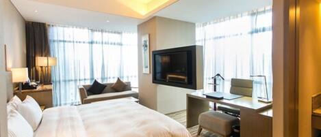 Quarto de hotel com uma cama grande, uma escrivaninha com cadeira, televisão e janela com cortinas.