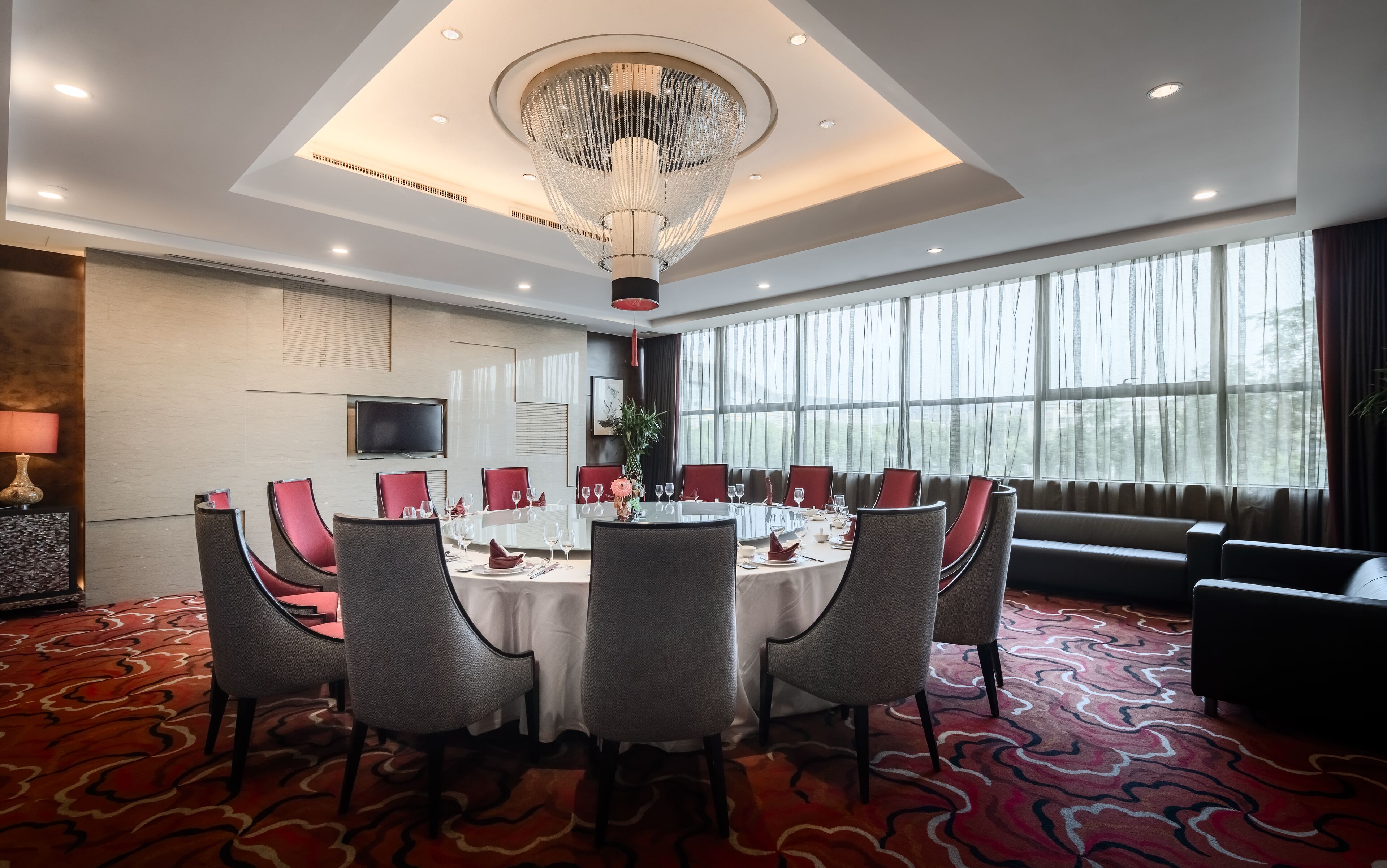 A hotel dining room with a round table set for six, surrounded by grey chairs.