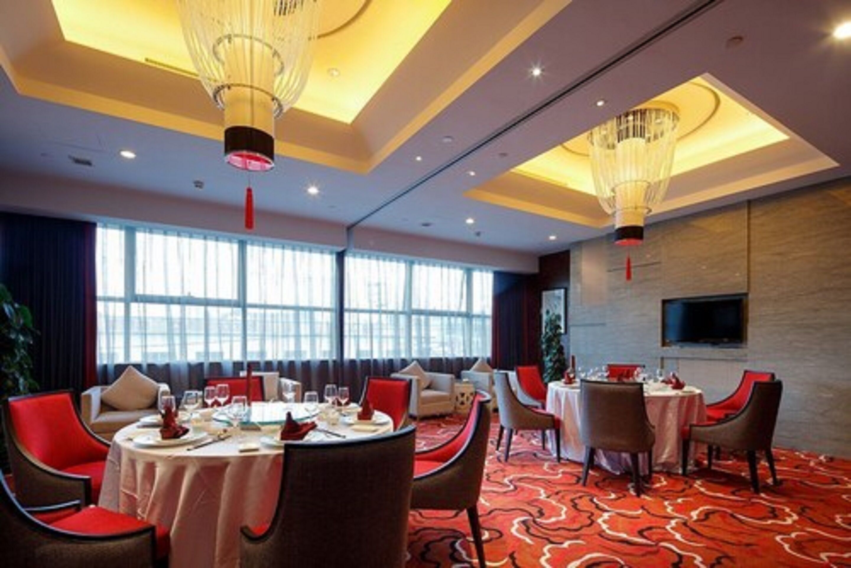 Ein Hotel-Speisesaal mit runden Tischen, roten Stühlen und Kronleuchtern.