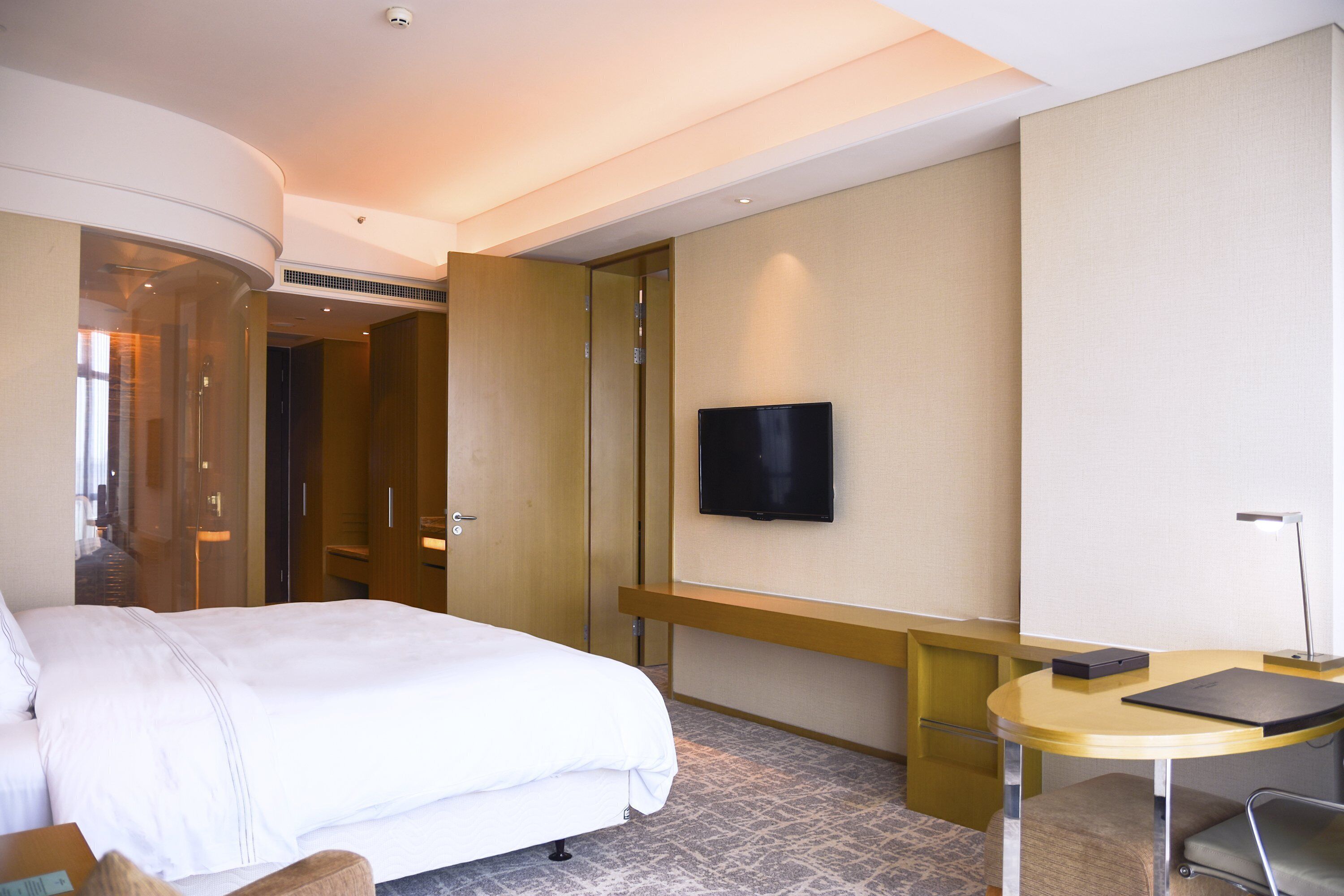 A hotel room with a bed, a desk, a chair, a television, and a door leading to another room.