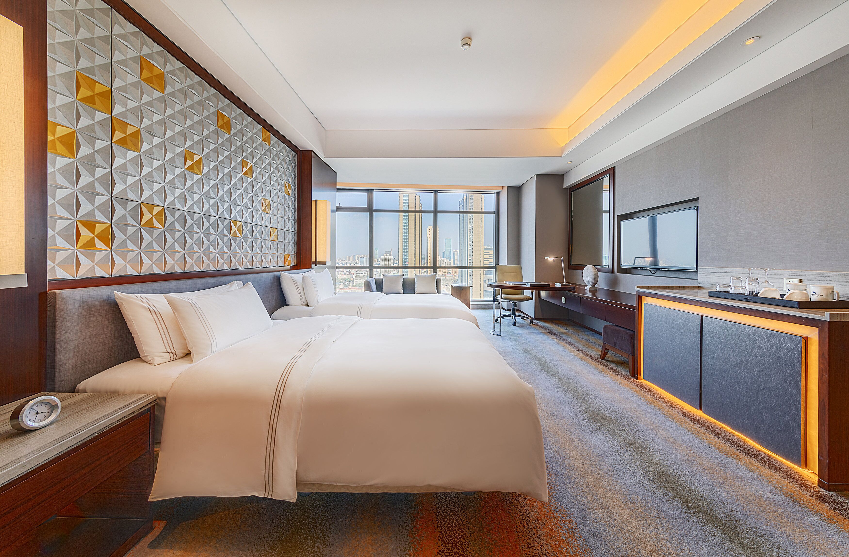Habitación de hotel con una cama grande, un escritorio con televisor y vistas al horizonte de la ciudad.