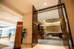 Vestíbulo de hotel con mostrador de recepción, una planta grande y un diseño de techo moderno.