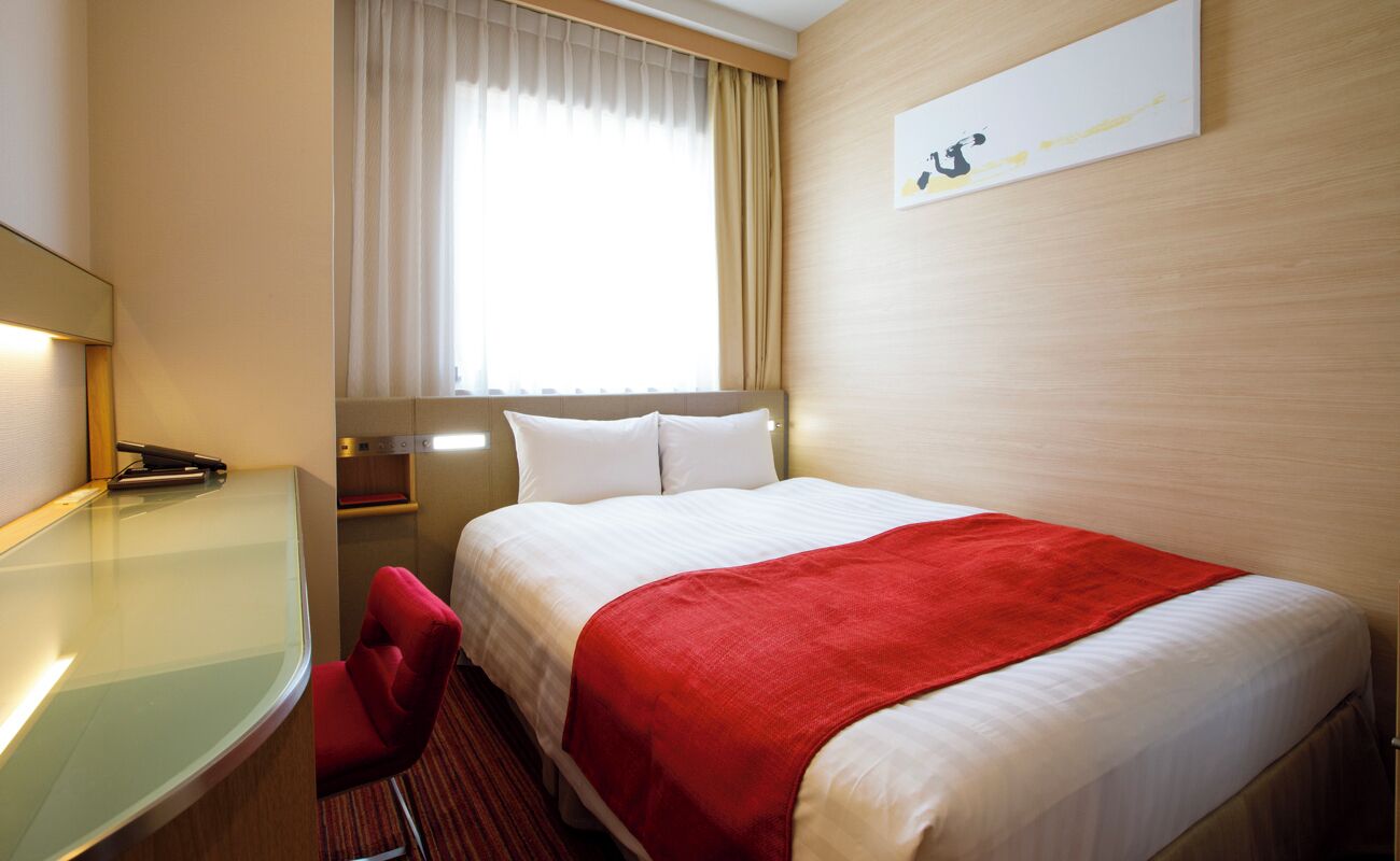 Hotelkamer met een bed, bureau, stoel, raam met gordijnen en een kunstwerk aan de muur.