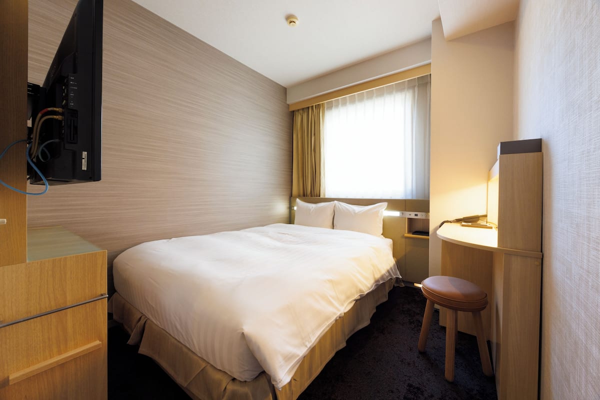 A hotel room with a bed, a desk, a chair, a television, and a window with curtains.