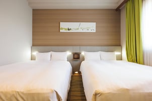 Habitación de hotel con dos camas, cabecero de madera, un cuadro sobre las camas y una cortina verde en la ventana.