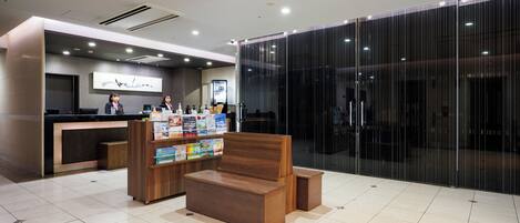 Un área de recepción moderna con un mostrador de madera, una zona de estar con un banco y un separador de vidrio.