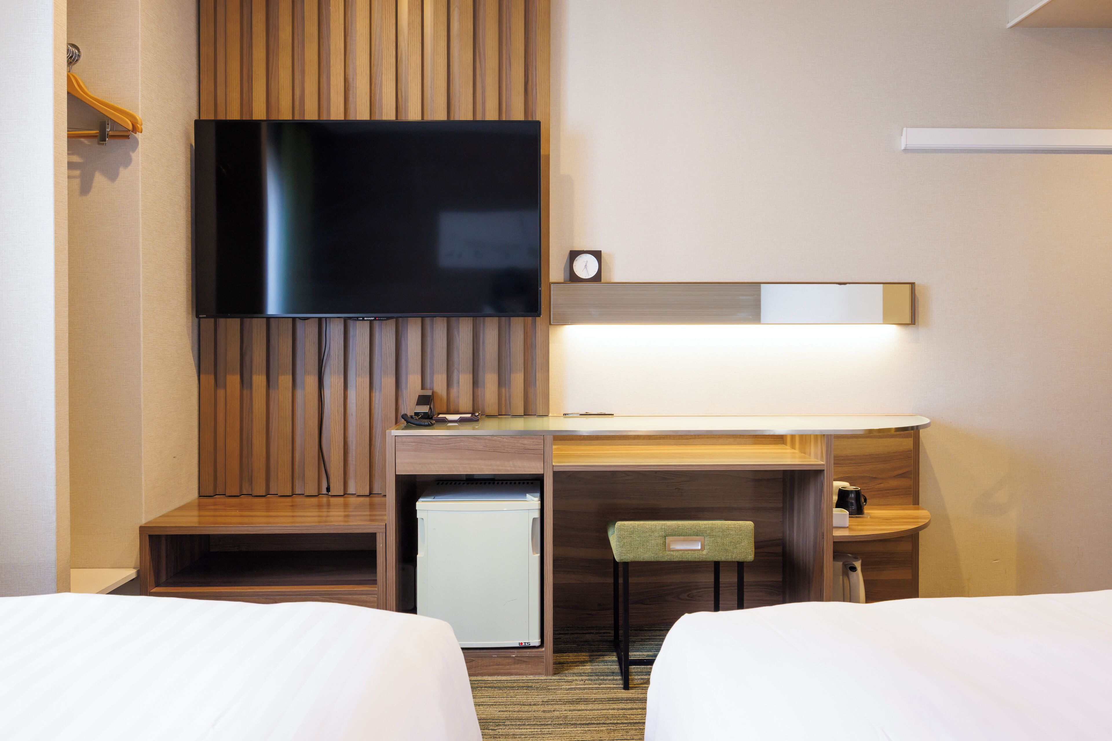Une chambre d’hôtel avec deux lits, une télévision, un bureau avec une chaise, un petit réfrigérateur et une table de chevet avec une lampe.