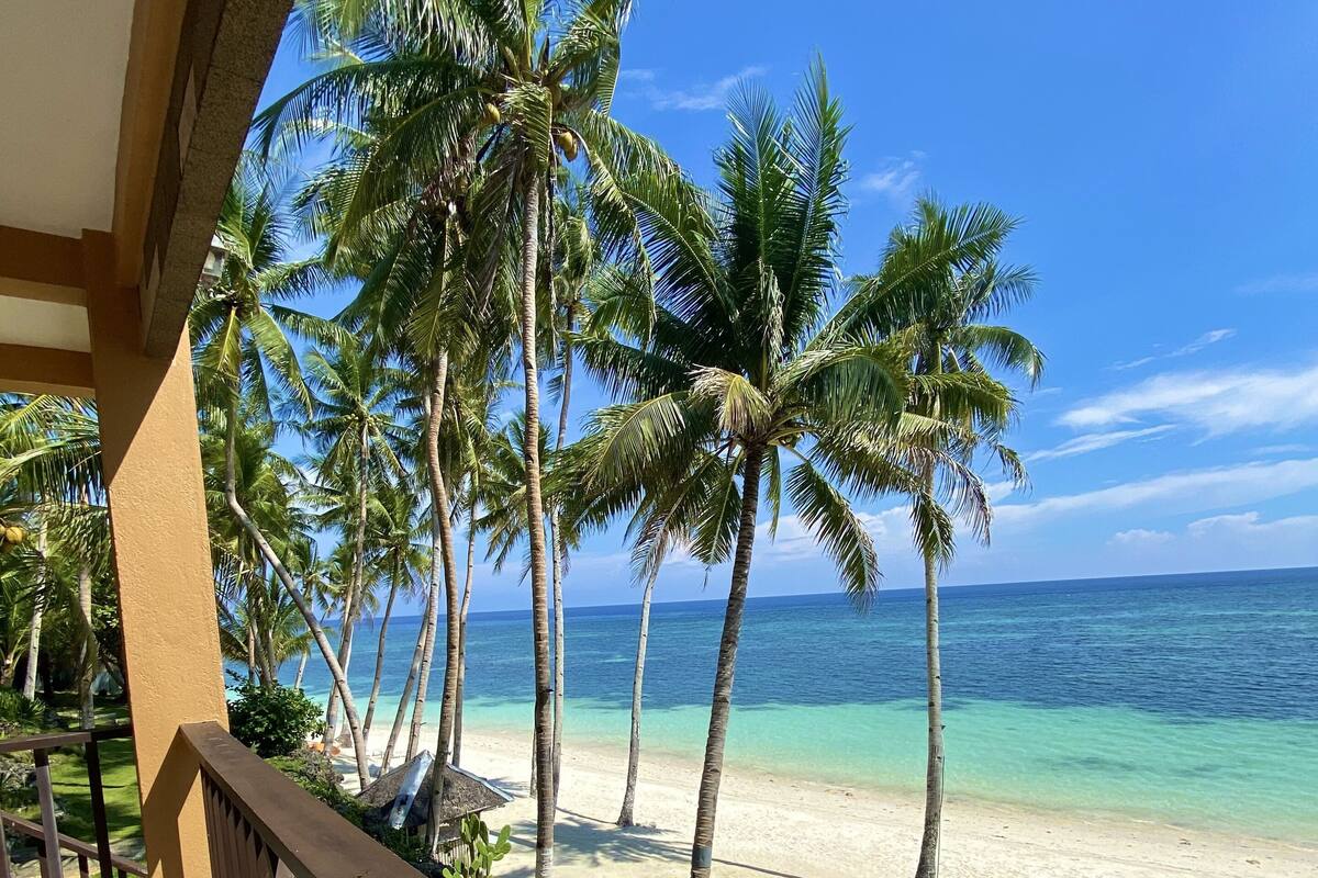 A balcony with a view of a beach, palm trees, and the ocean.