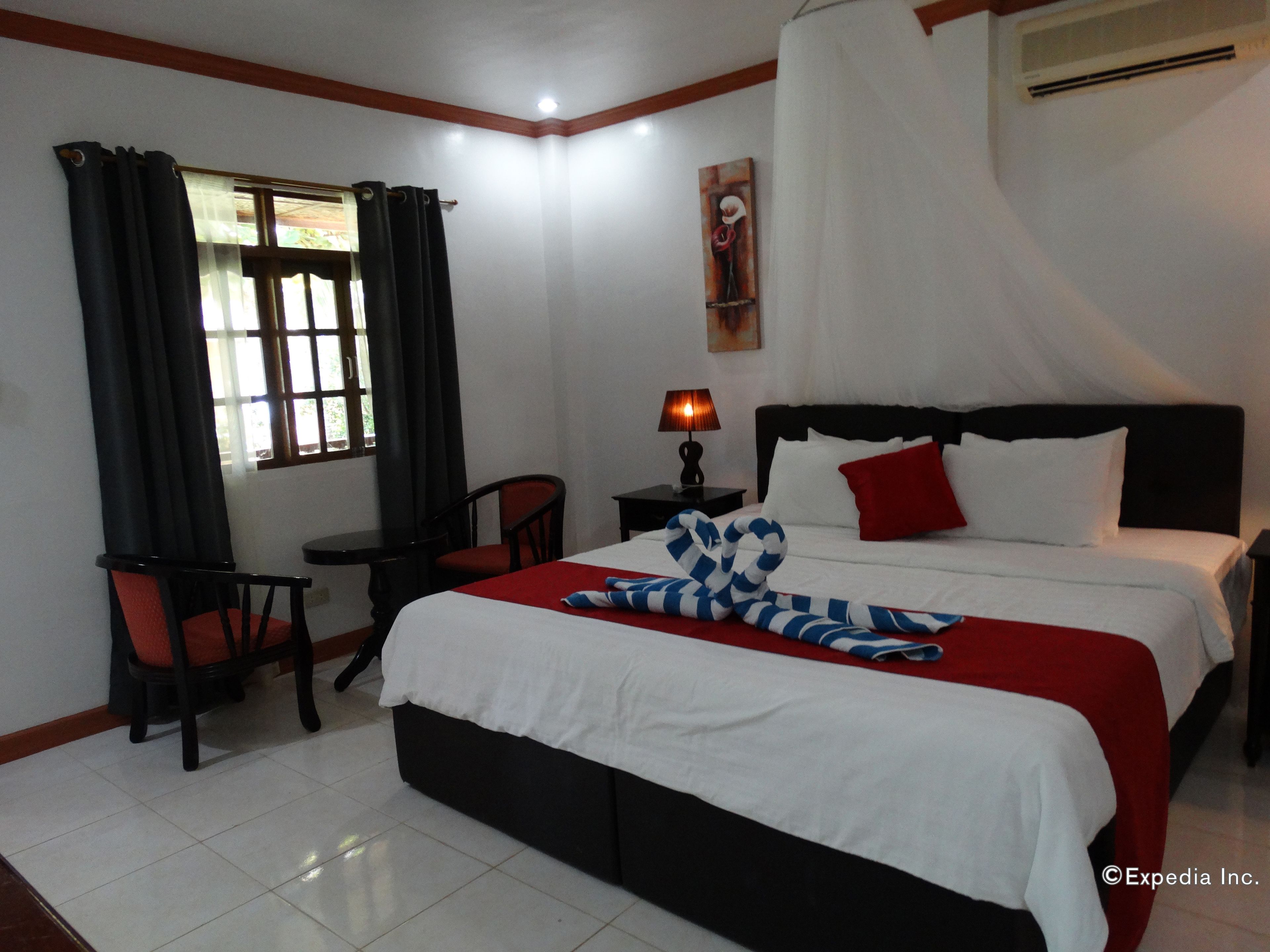 A hotel room with a bed, a chair, a table, a lamp, and a window with curtains.