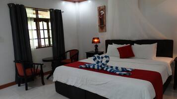 A hotel room with a bed, a chair, a table, a lamp, and a window with curtains.