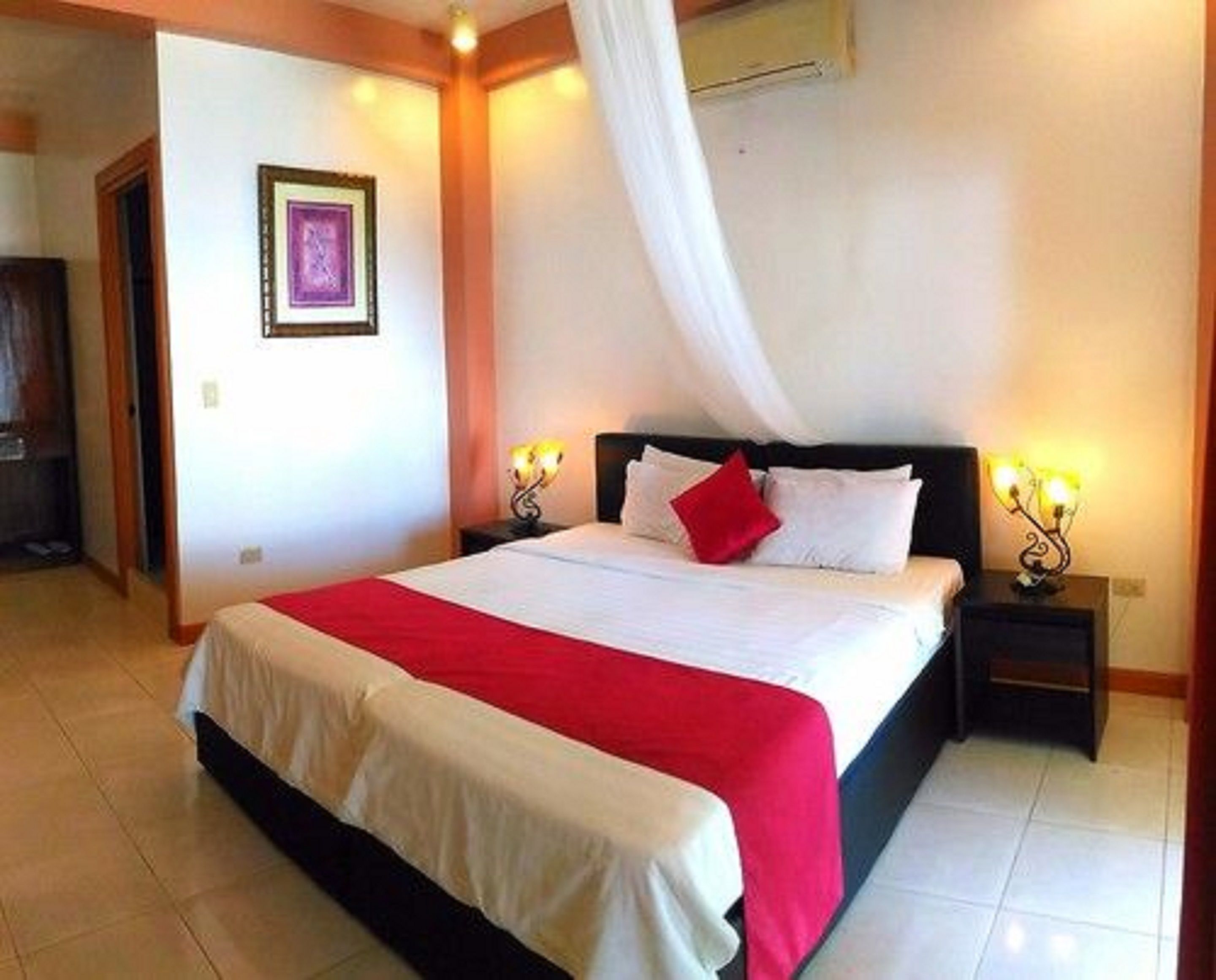 Una habitación de hotel con una cama grande, ropa de cama blanca, un plaid rojo y dos lámparas de noche.