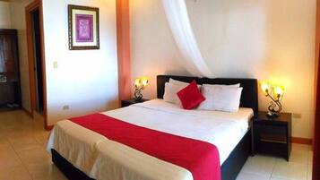 Una habitación de hotel con una cama grande, ropa de cama blanca, un plaid rojo y dos lámparas de noche.