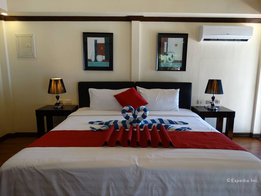 Hotelkamer met een bed, twee nachtkastjes, twee lampen, een rood-wit gestreepte deken en twee ingelijste kunstwerken aan de muur.