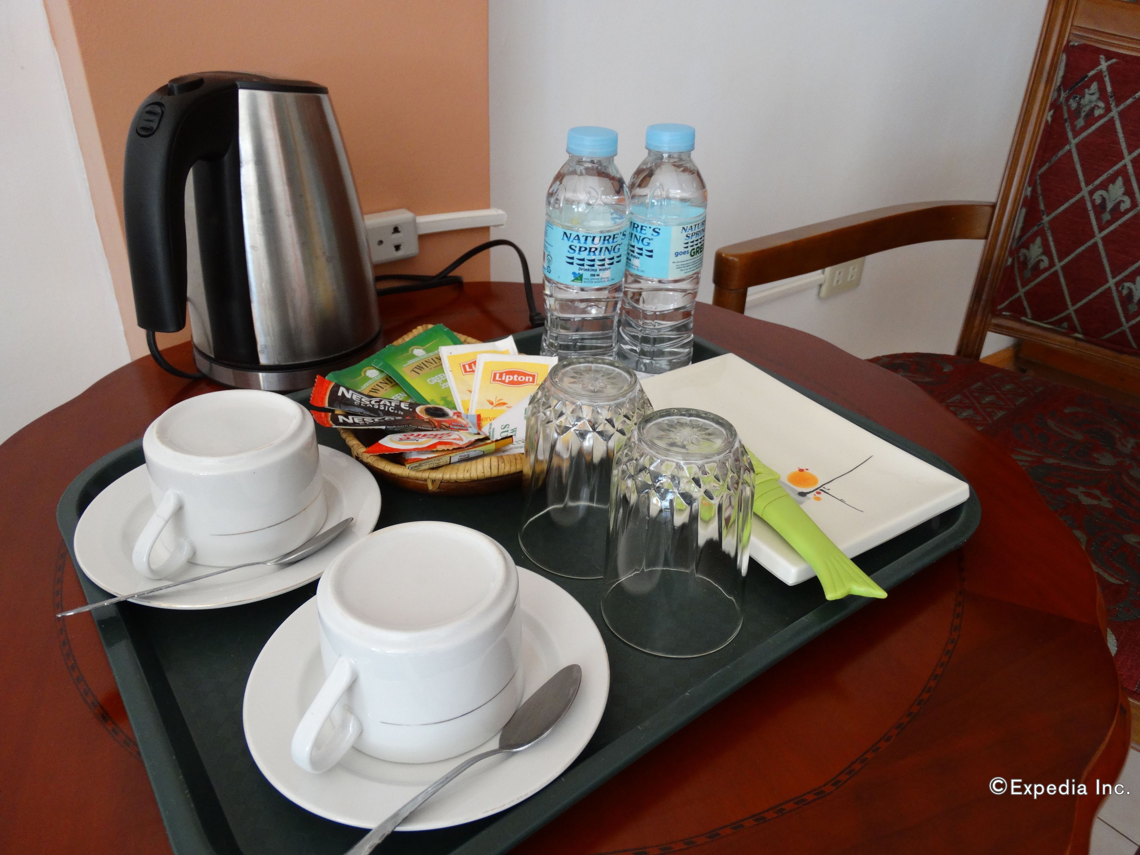 Una bandeja con dos tazas blancas, una tetera, botellas de agua y una cesta de aperitivos.