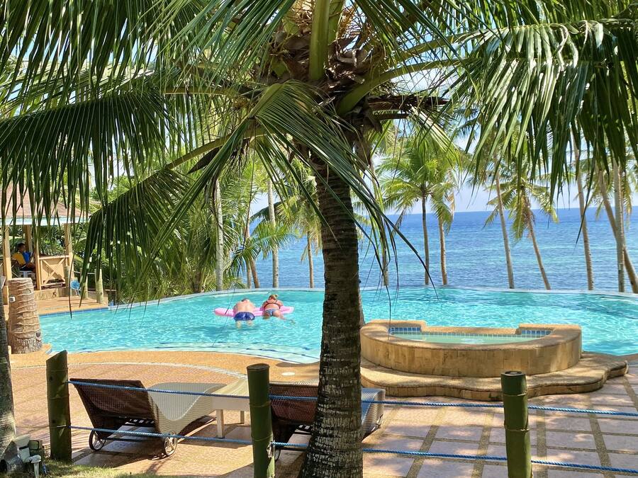 Un área de piscina con vistas al océano, palmeras y sillas de descanso.