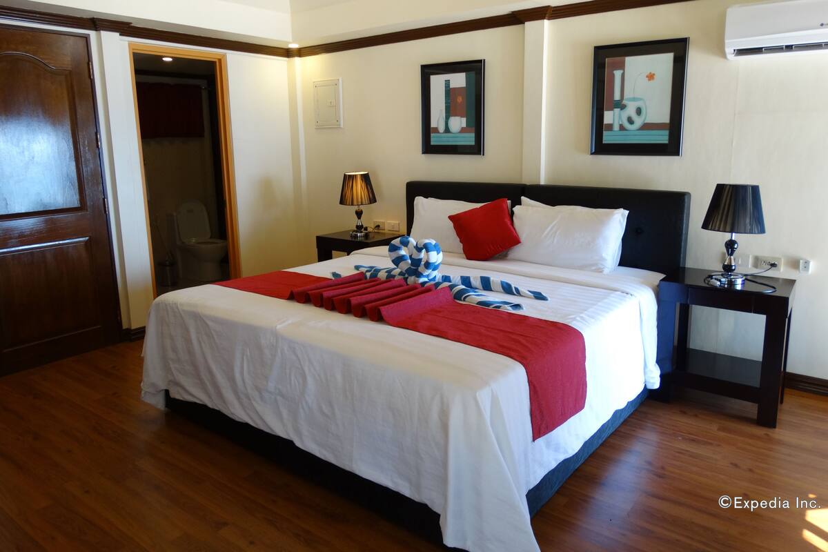 A hotel room with a large bed, a nightstand, a lamp, and a picture on the wall.