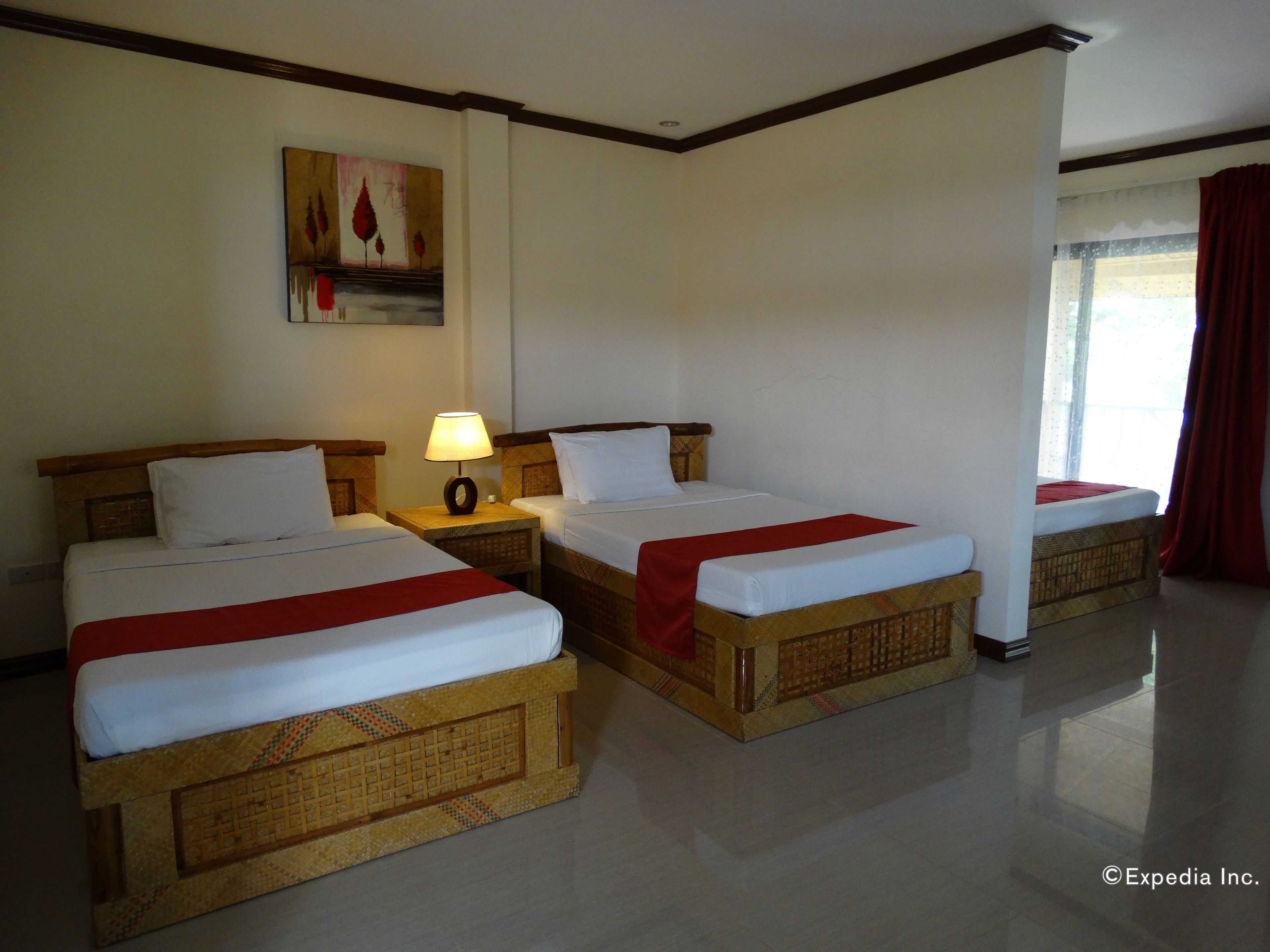 Quarto de hotel com duas camas, uma mesinha de cabeceira com abajur, um quadro na parede e uma janela com cortinas.
