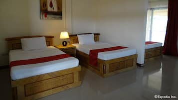 Quarto de hotel com duas camas, uma mesinha de cabeceira com abajur, um quadro na parede e uma janela com cortinas.