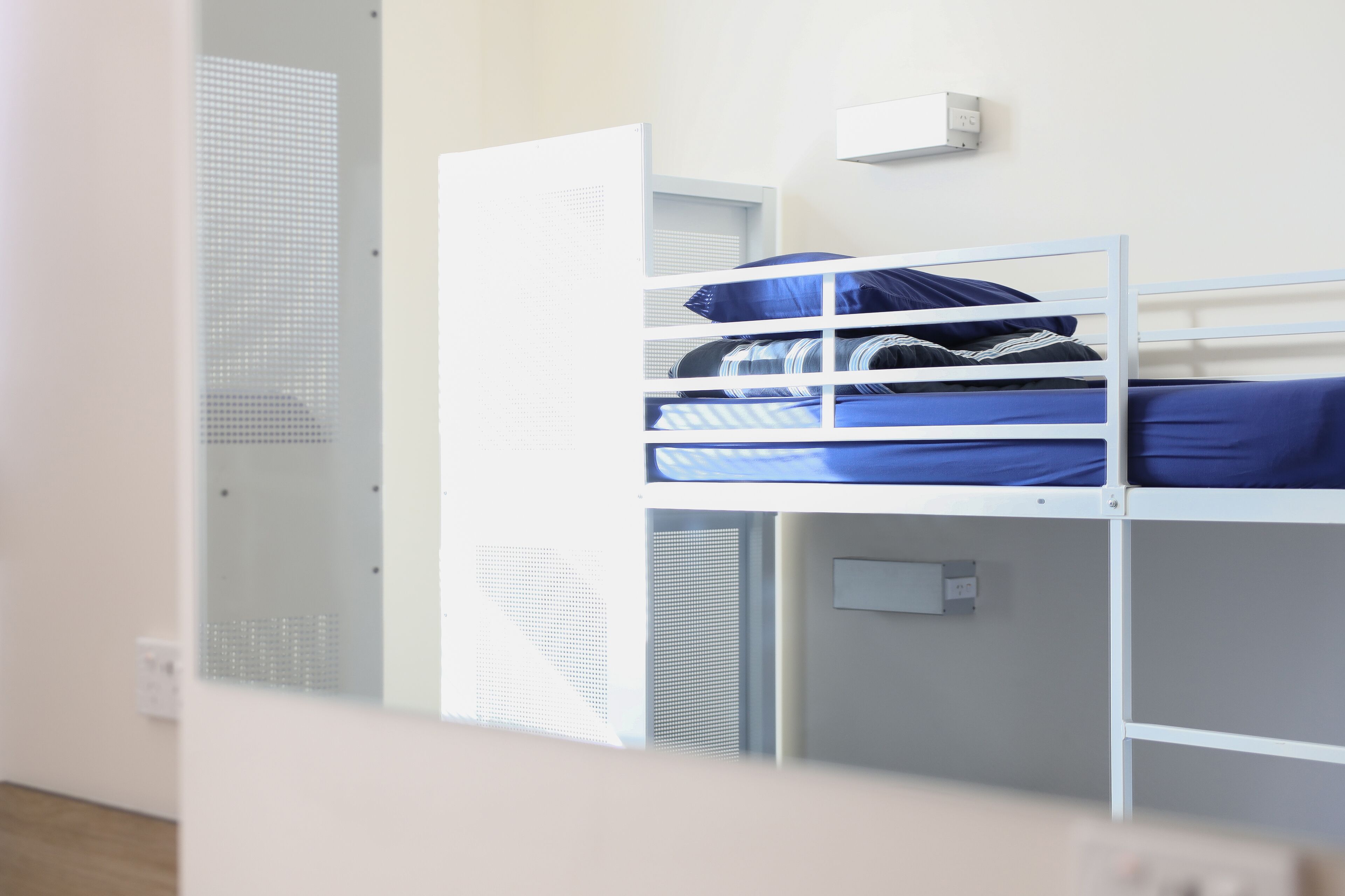 Una cama litera con estructura metálica blanca y ropa de cama azul.