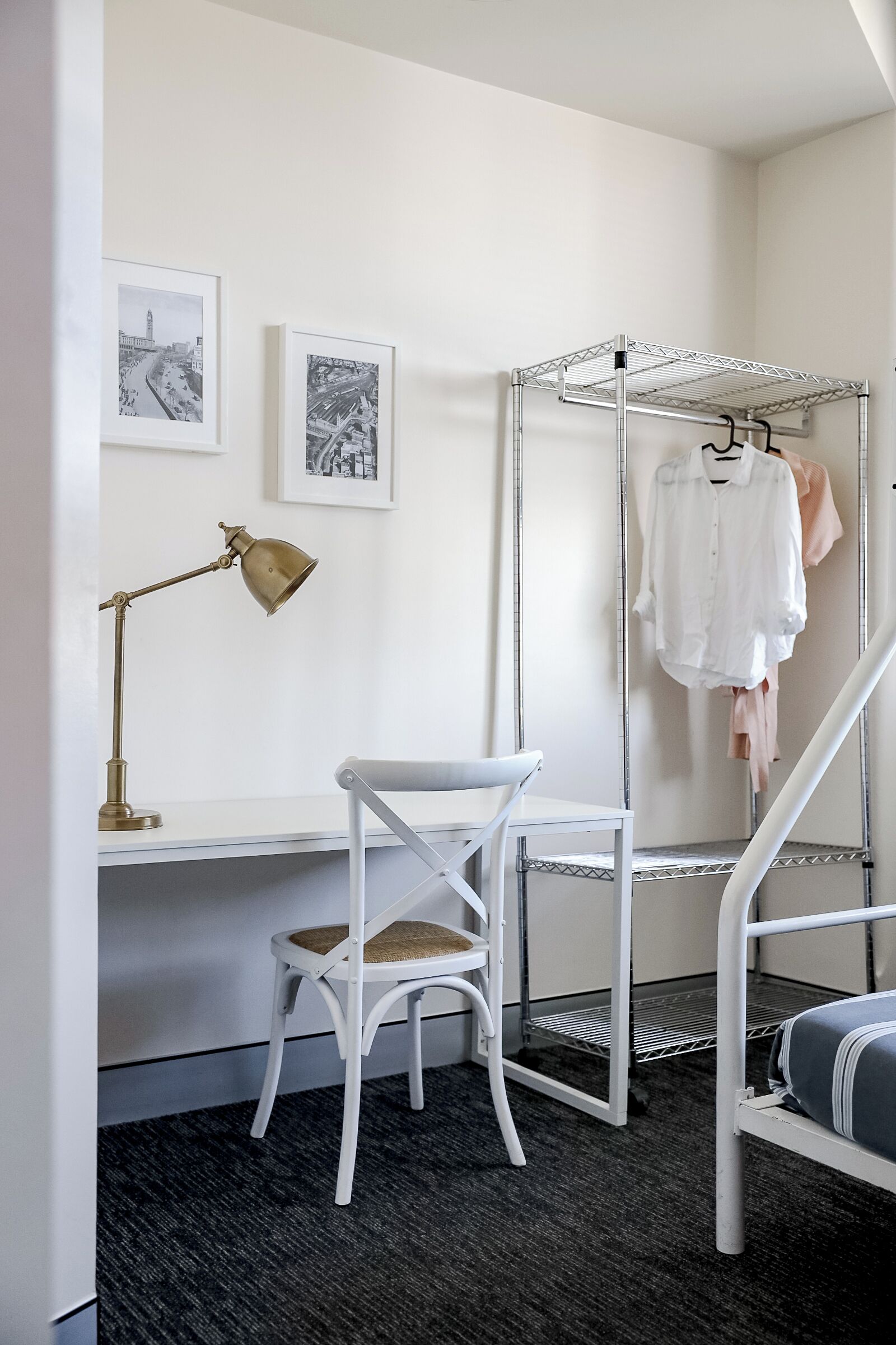 A room with a desk, a chair, a metal rack with clothes, and framed pictures on the wall.