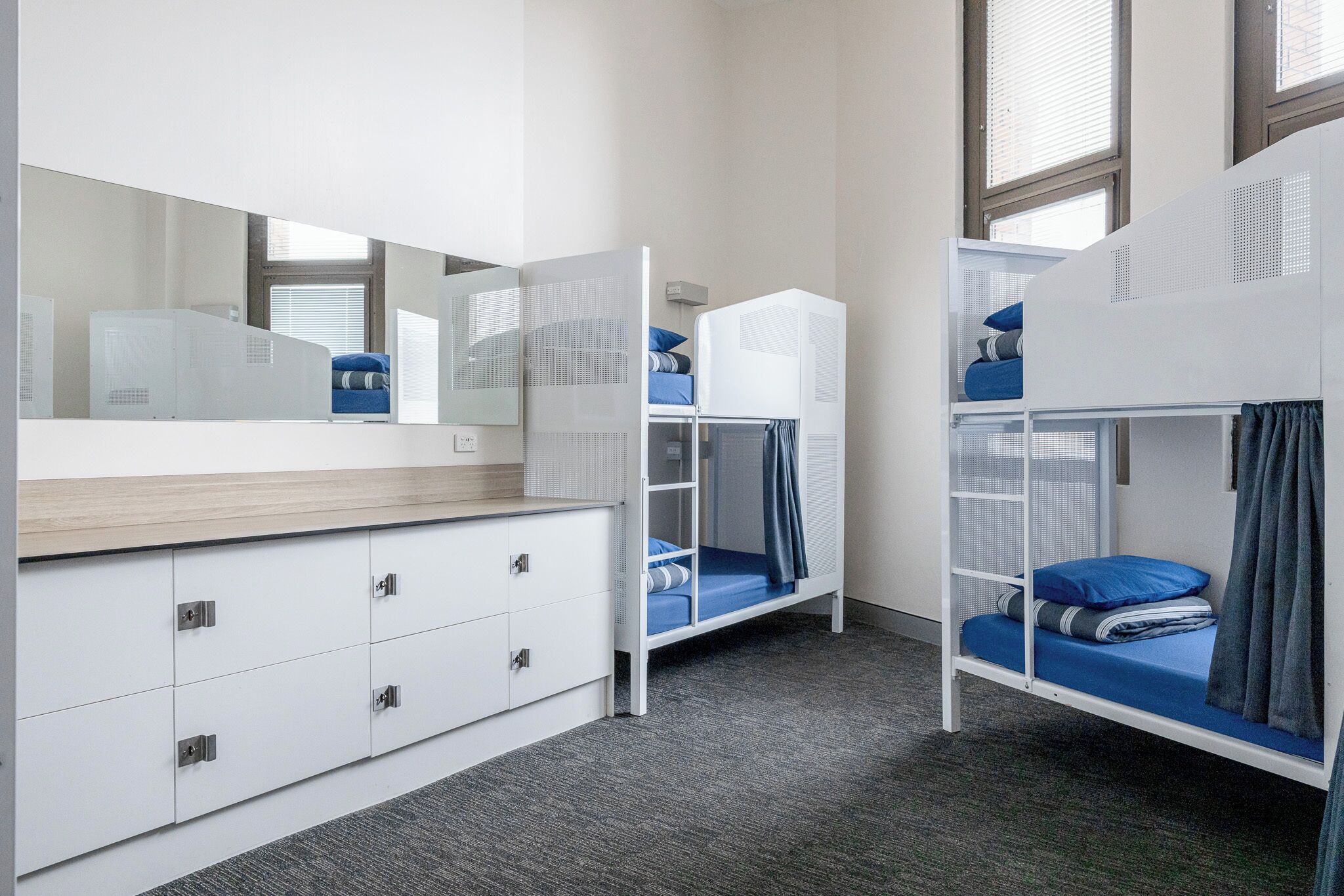 Ein Zimmer mit Etagenbetten, einer Kommode mit Schubladen, einem Spiegel und einem Fenster.