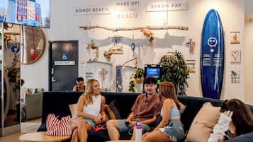 A group of people sitting on a couch in a room with a beach-themed decor, including a surfboard and a sign that says 'Wake Up! - At the Beach'.