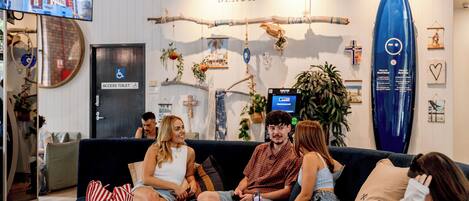 A group of people sitting on a couch in a room with a beach-themed decor, including a surfboard and a sign that says 'Wake Up! - At the Beach'.