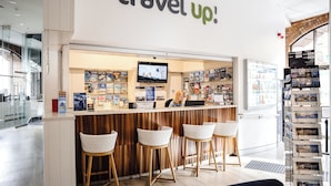 A travel agency counter with a wooden panel design, a TV screen, and a display of travel brochures. - Wake Up! Sydney - Hostel (Haymarket)