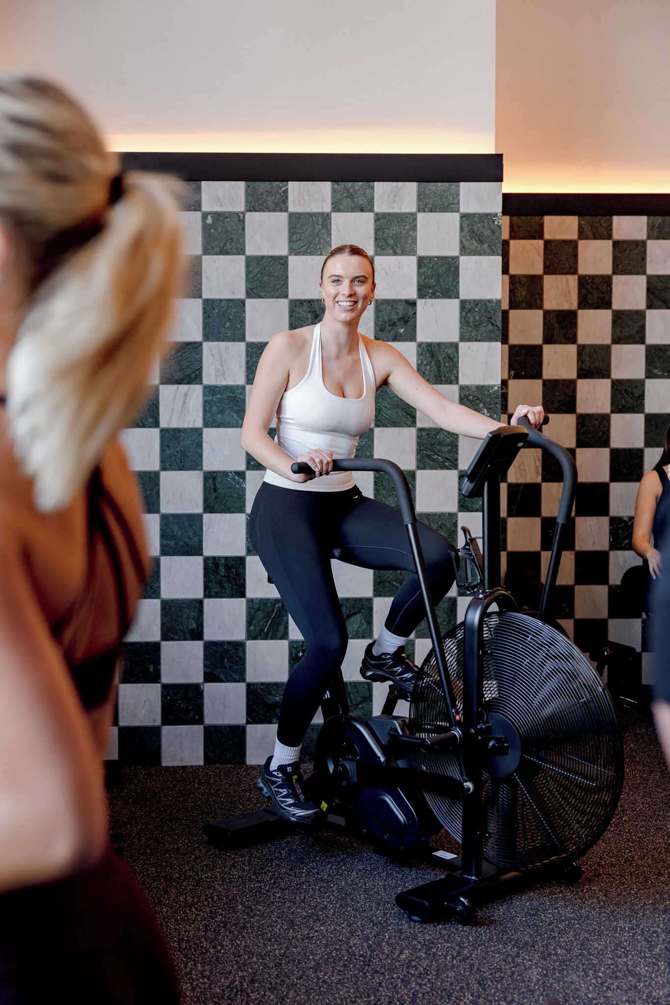A person using an exercise bike in a room with a checkered floor pattern.
