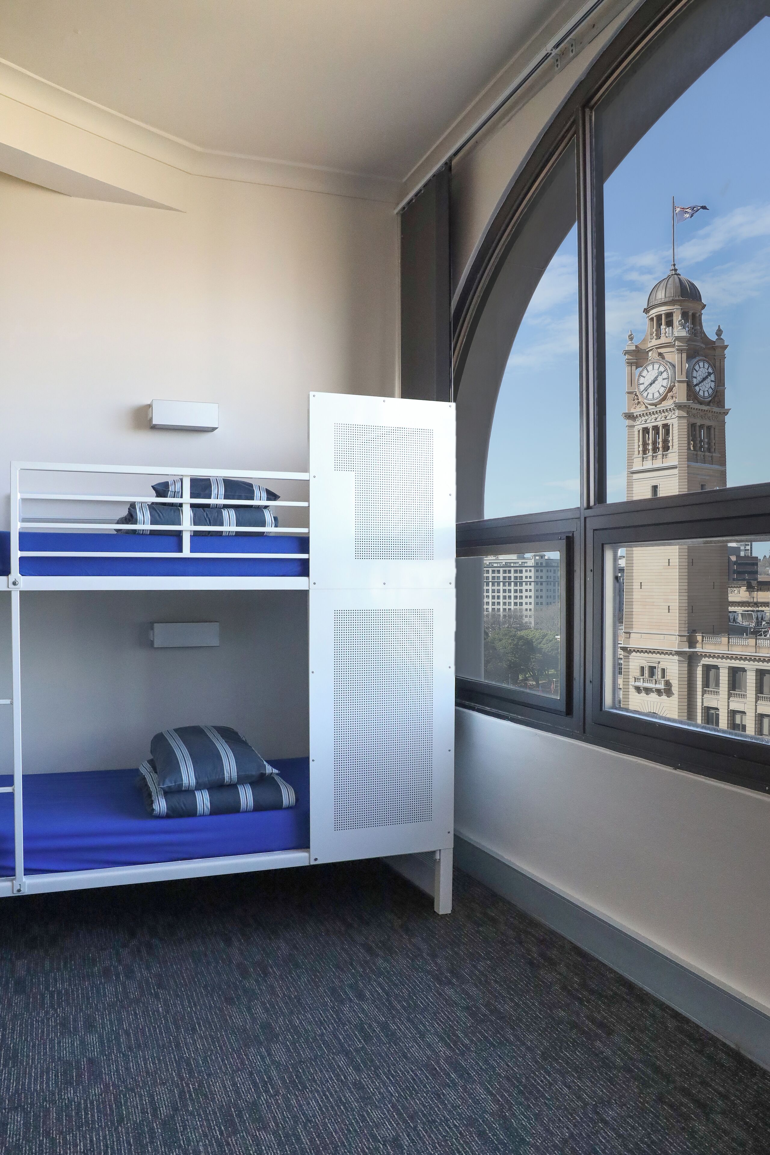 A bunk bed room with a large window offering a view of a clock tower.