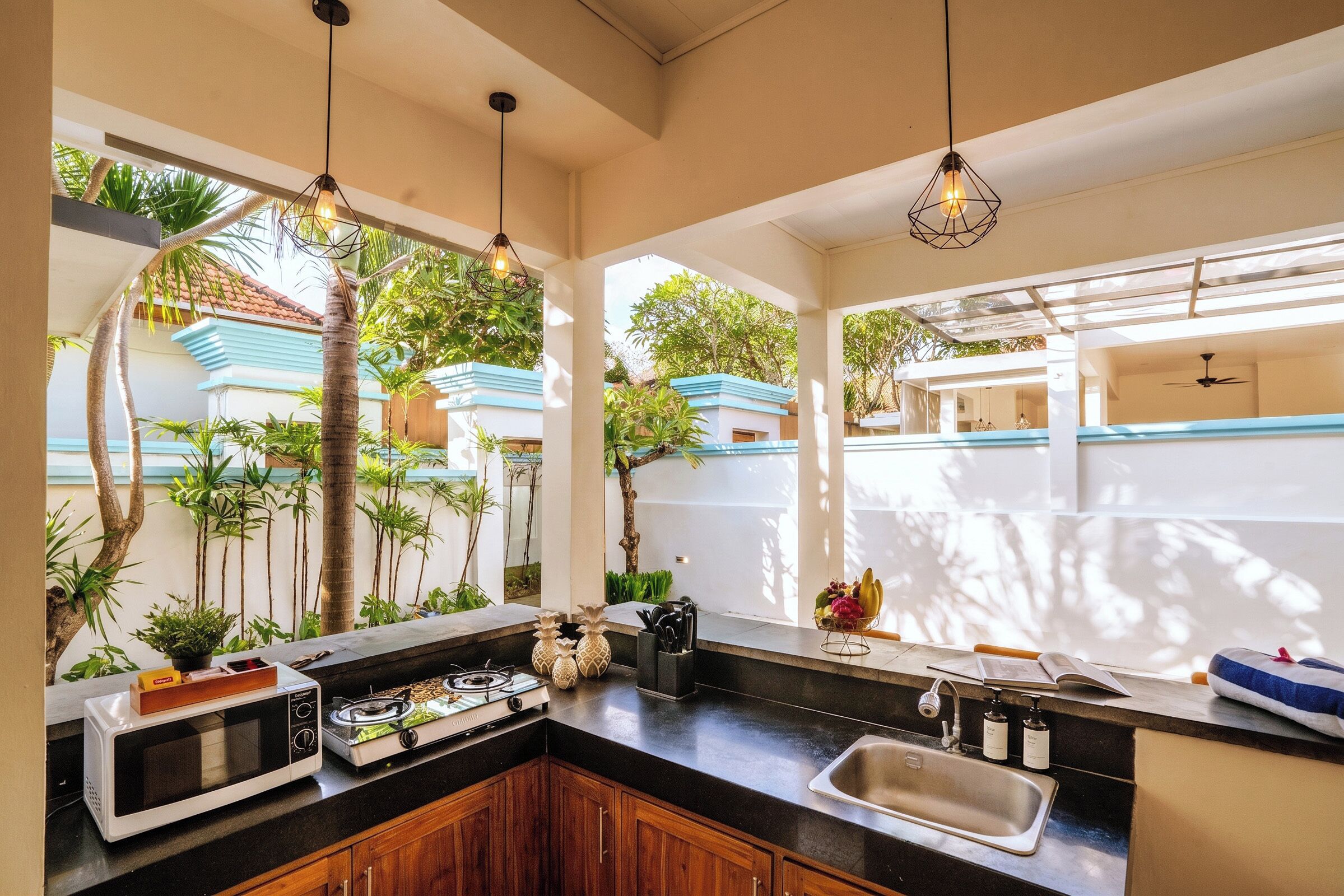 A kitchen with a built-in microwave, stove, and sink, with a view of a blue house and greenery outside.