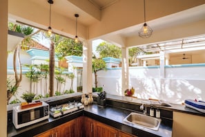A kitchen with a built-in microwave, stove, and sink, with a view of a blue house and greenery outside. - Villa Kisaraa (Kerobokan)