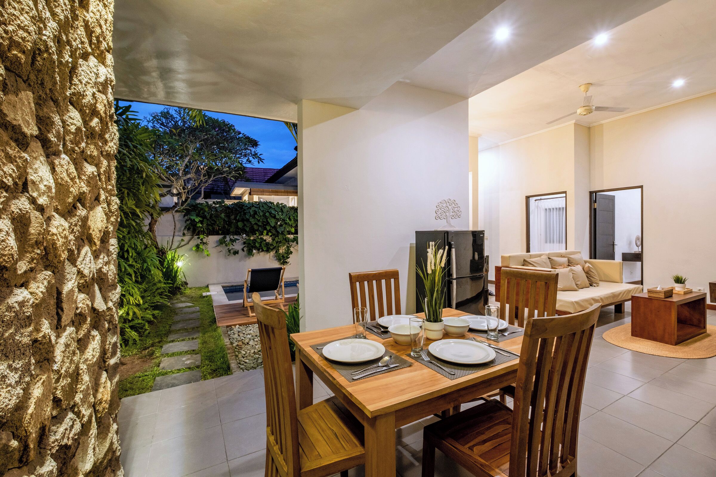 Un comedor moderno con una mesa preparada para cuatro, un sofá y una zona de cocina con refrigerador y estufa.
