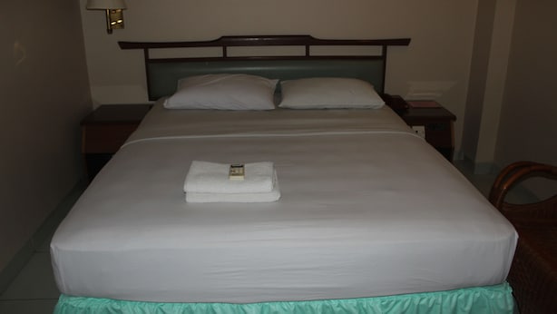 A neatly made bed with a white blanket and a folded towel on top, a wooden headboard, and a bedside lamp. - Batam Star Hotel (Batam)