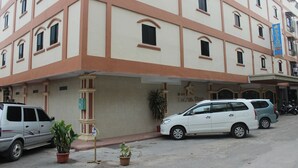 A multi-story hotel with a beige facade and brown trim. There are several cars parked in front, and a few potted plants are visible on the sidewalk. - Batam Star Hotel (Batam)