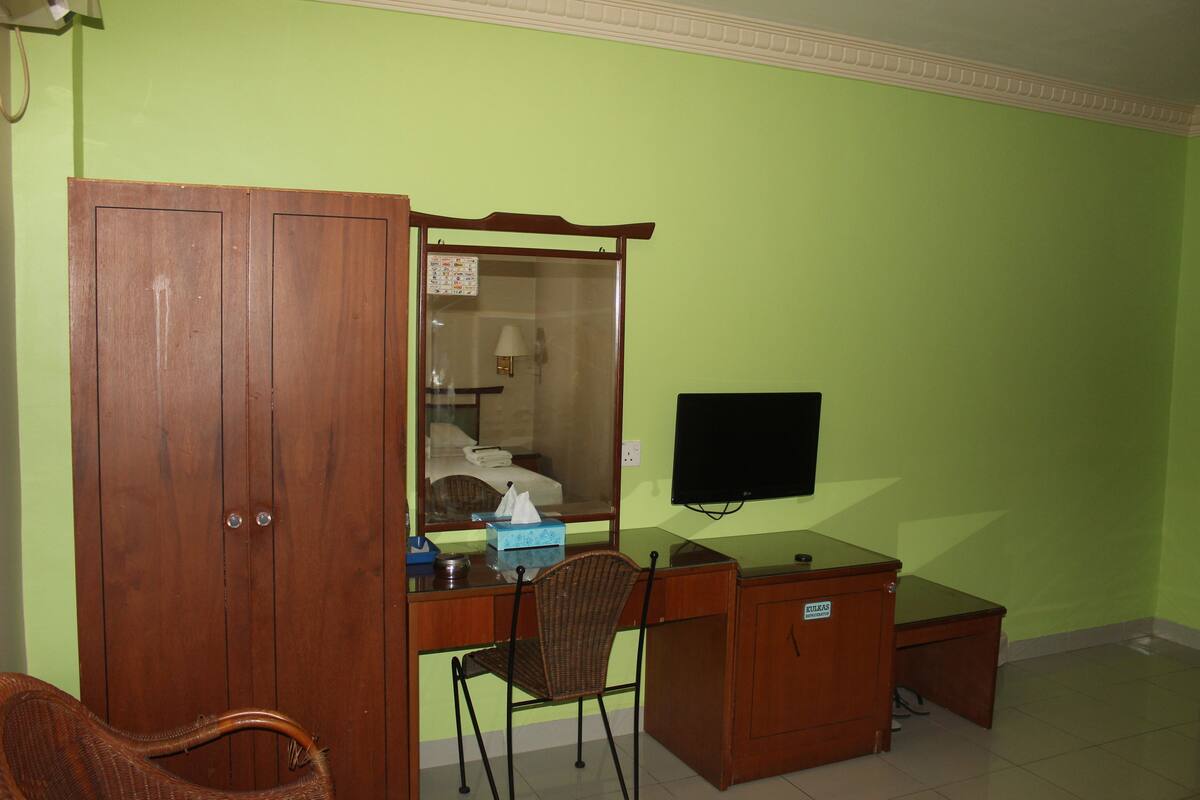 Una habitación con un escritorio de madera, una silla de mimbre, un armario y un televisor en la pared.