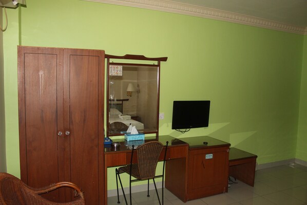 Une pièce avec un bureau en bois, une chaise en osier, une armoire et un téléviseur fixé au mur.