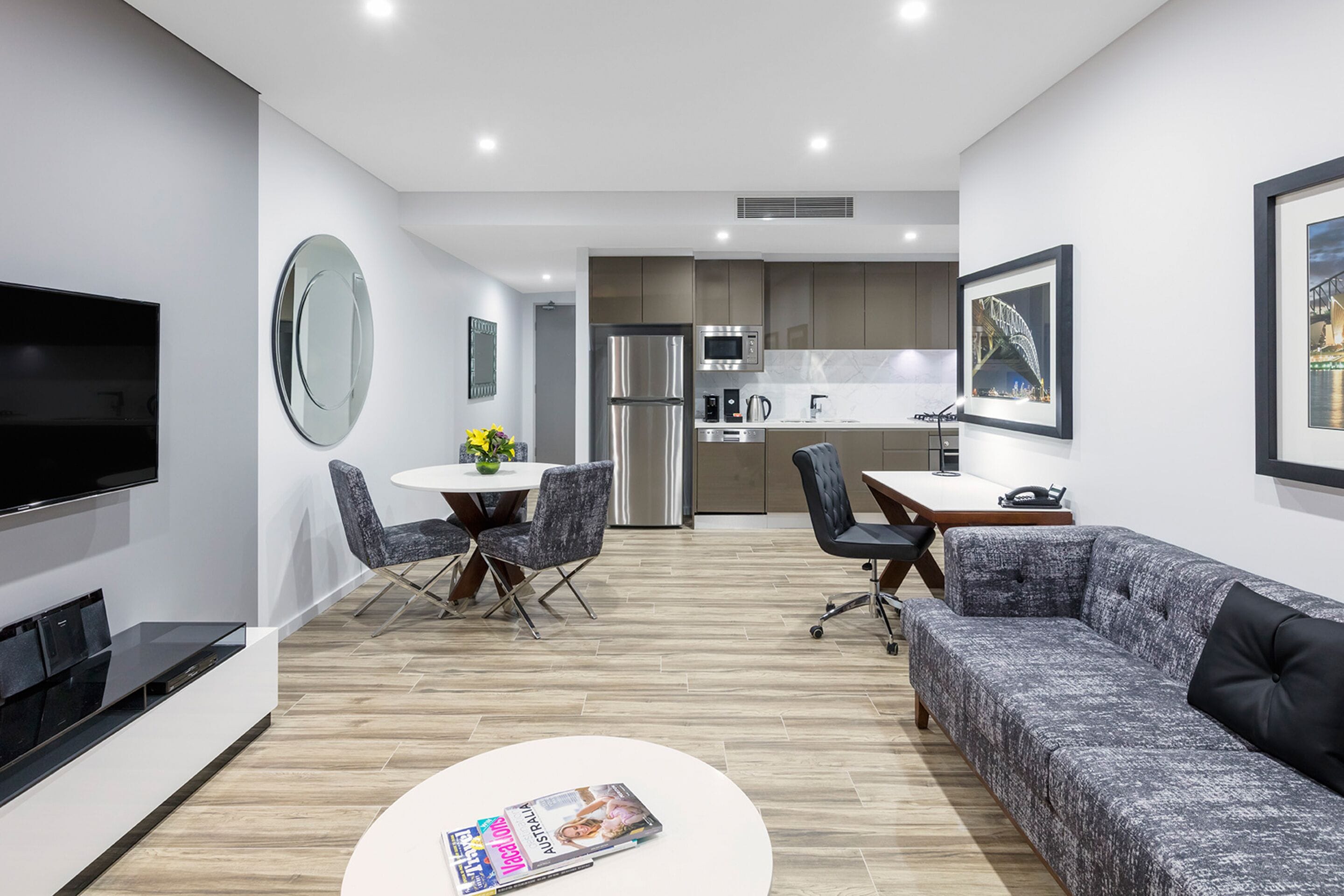 A modern living room with a flat-screen TV, a sofa, a coffee table, and a dining area with chairs and a table.
