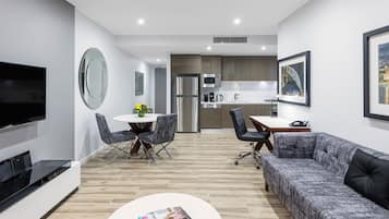 A modern living room with a flat-screen TV, a sofa, a coffee table, and a dining area with chairs and a table.