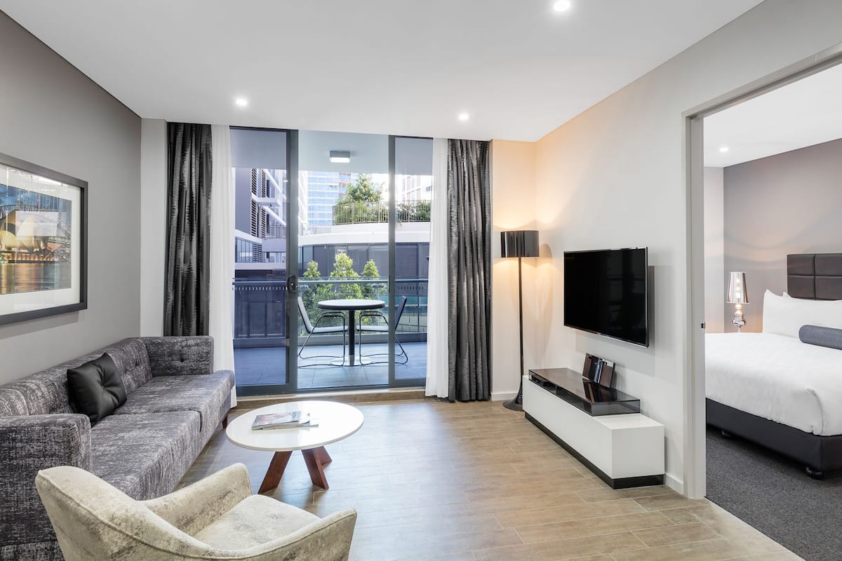 Una habitación de hotel moderna con sofá, sillón, televisor de pantalla plana y cama.