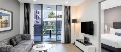 Een moderne hotelkamer met een bank, fauteuil, flatscreen televisie en een bed.