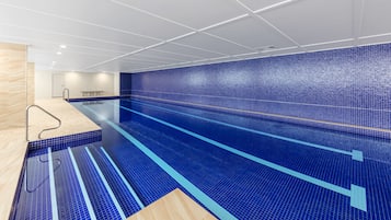 A modern indoor swimming pool with blue tiled walls and a wooden floor.