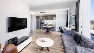 A modern living room with a flat-screen TV, a sofa, a coffee table, and a dining area with a table and chairs.