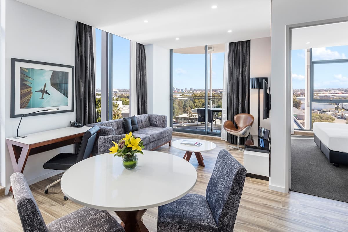 Una habitación de hotel moderna con un ventanal grande, un sofá, una mesa de comedor y una cama.