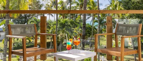 A balcony with two wooden chairs and a small table, each with a drink and a straw.