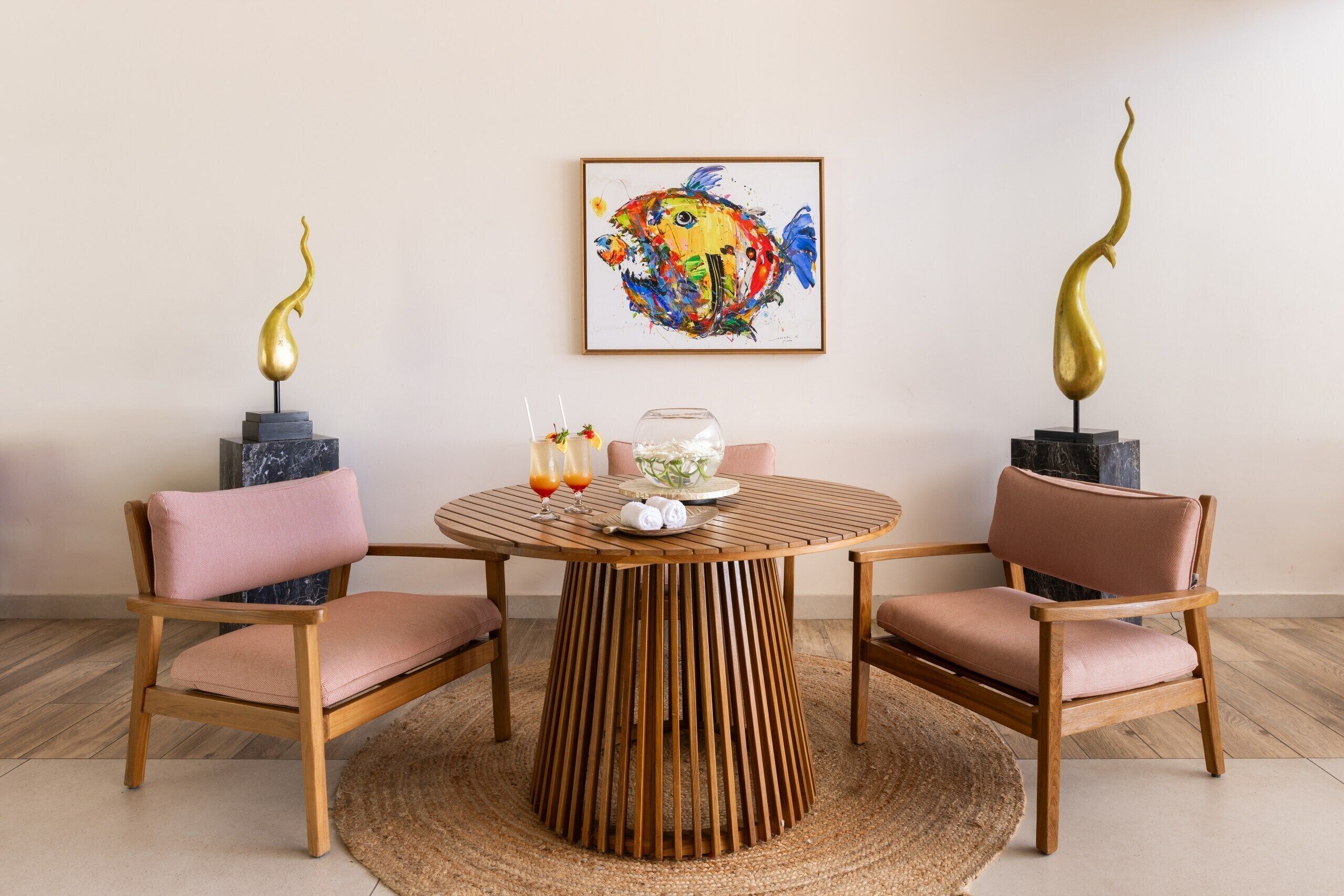 A dining area with a round wooden table, two cushioned chairs, and a colorful fish painting on the wall.