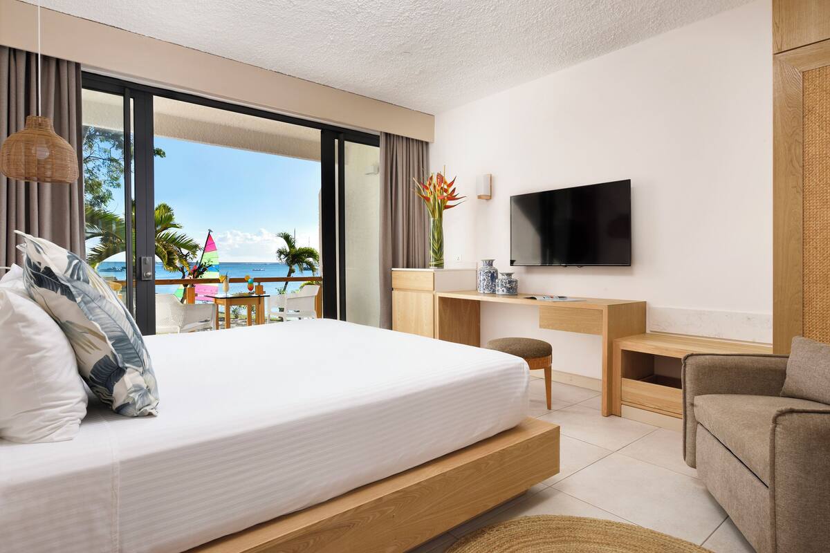 Una habitación de hotel moderna con cama, escritorio, televisor y vista a la playa.